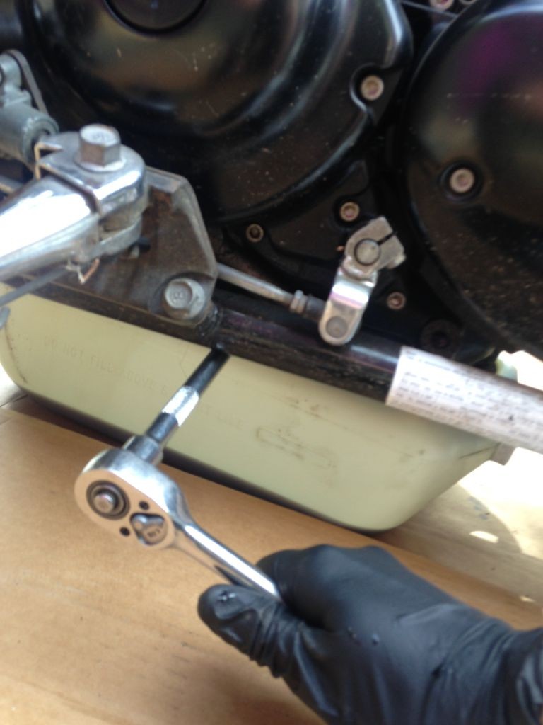 The oil drain bolt is reached on the left side of the bike, beneath the frame rail, on the left side of the oil pan. 